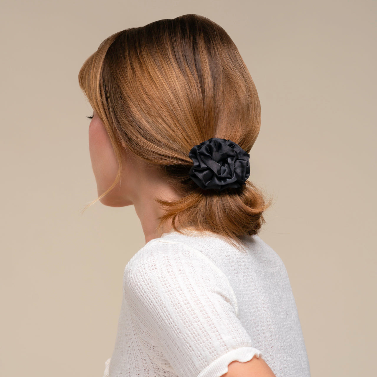 Person with a kitsch black rosette ruched scrunchie in their hair against a beige background